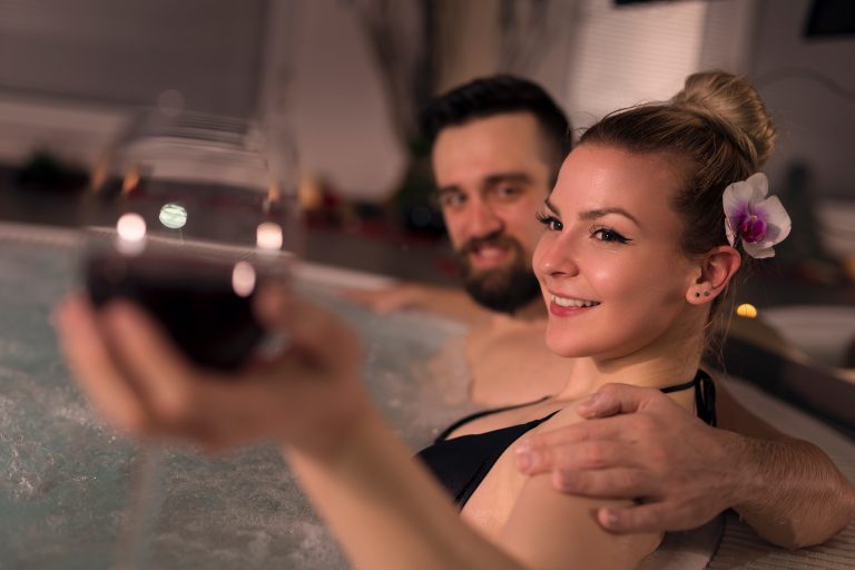 Couple in love enjoying the romantic atmosphere of a jacuzzi bath, drinking wine and relaxing